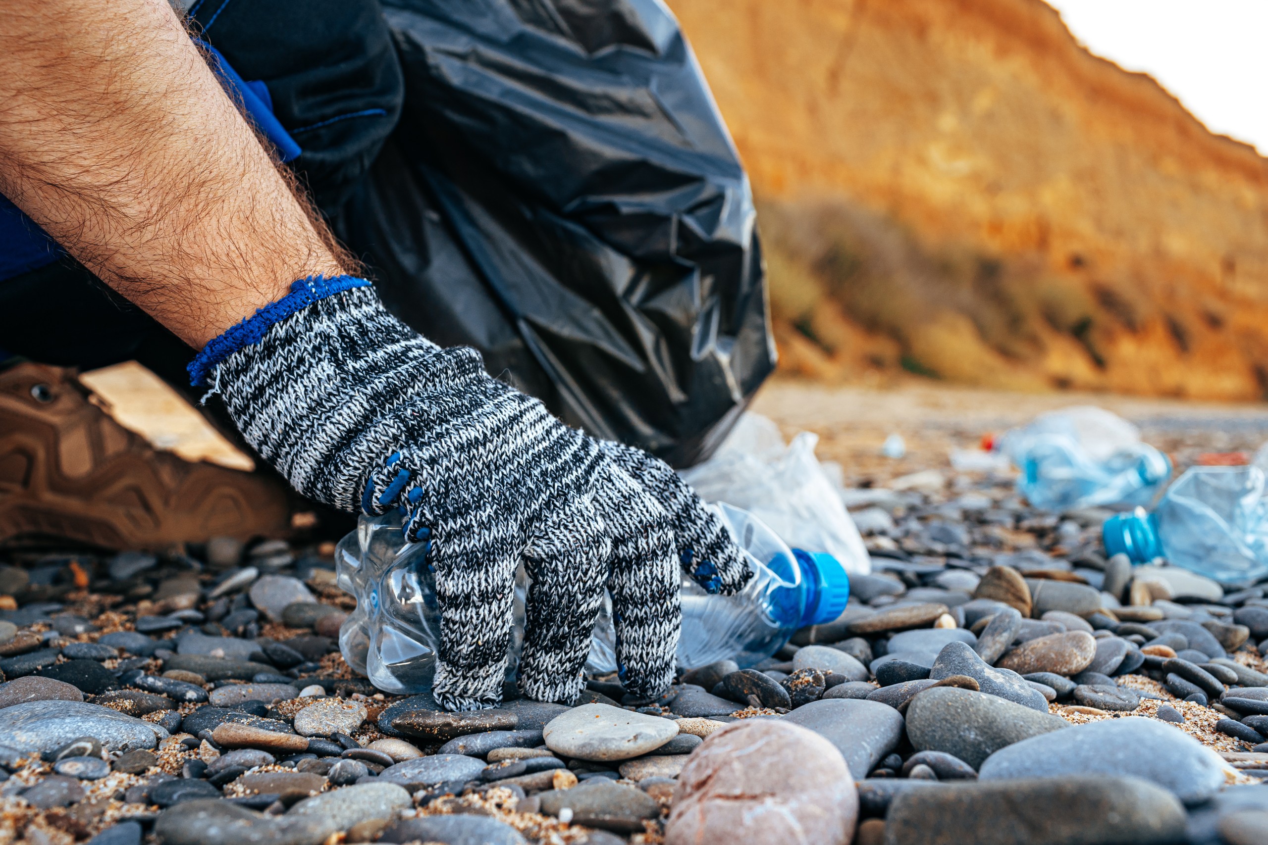 Freiwilliger sammelt mit Handschuhen Plastikmüll an einem Steinstrand